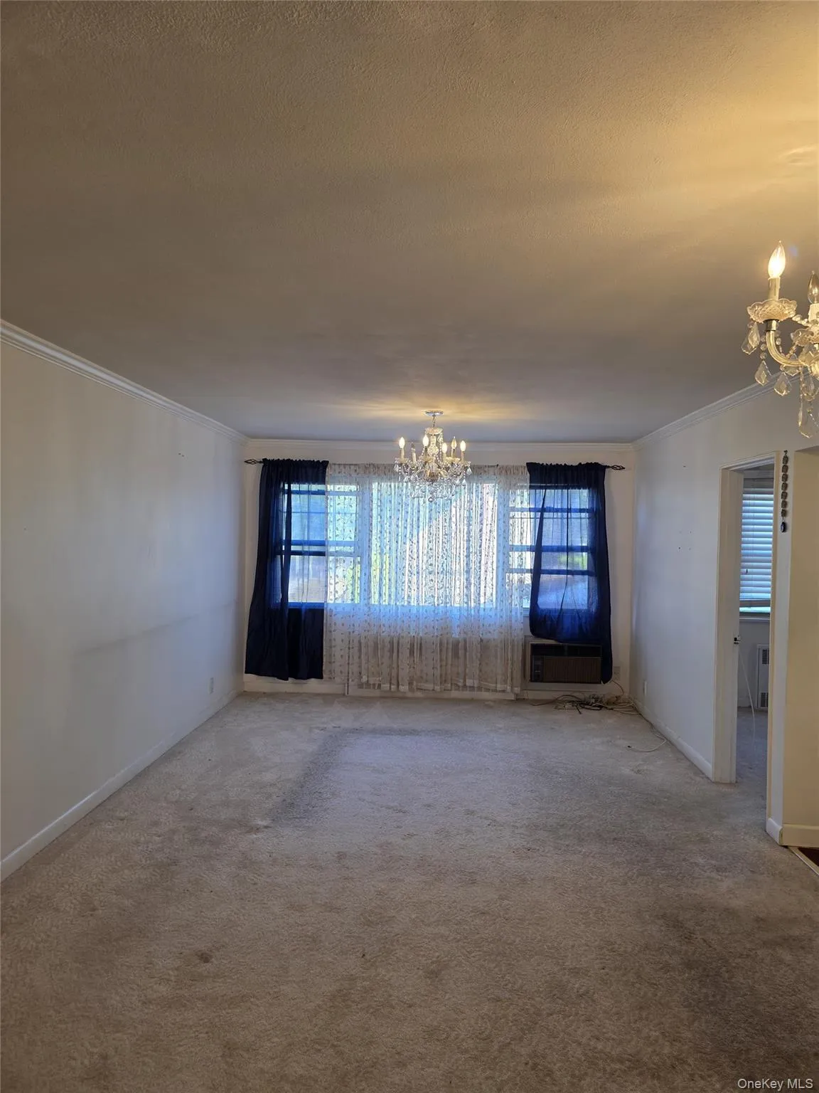 Carpeted empty room featuring a chandelier, crown molding, and cooling unit Carpeted empty room featuring a chandelier, crown molding, and cooling unit