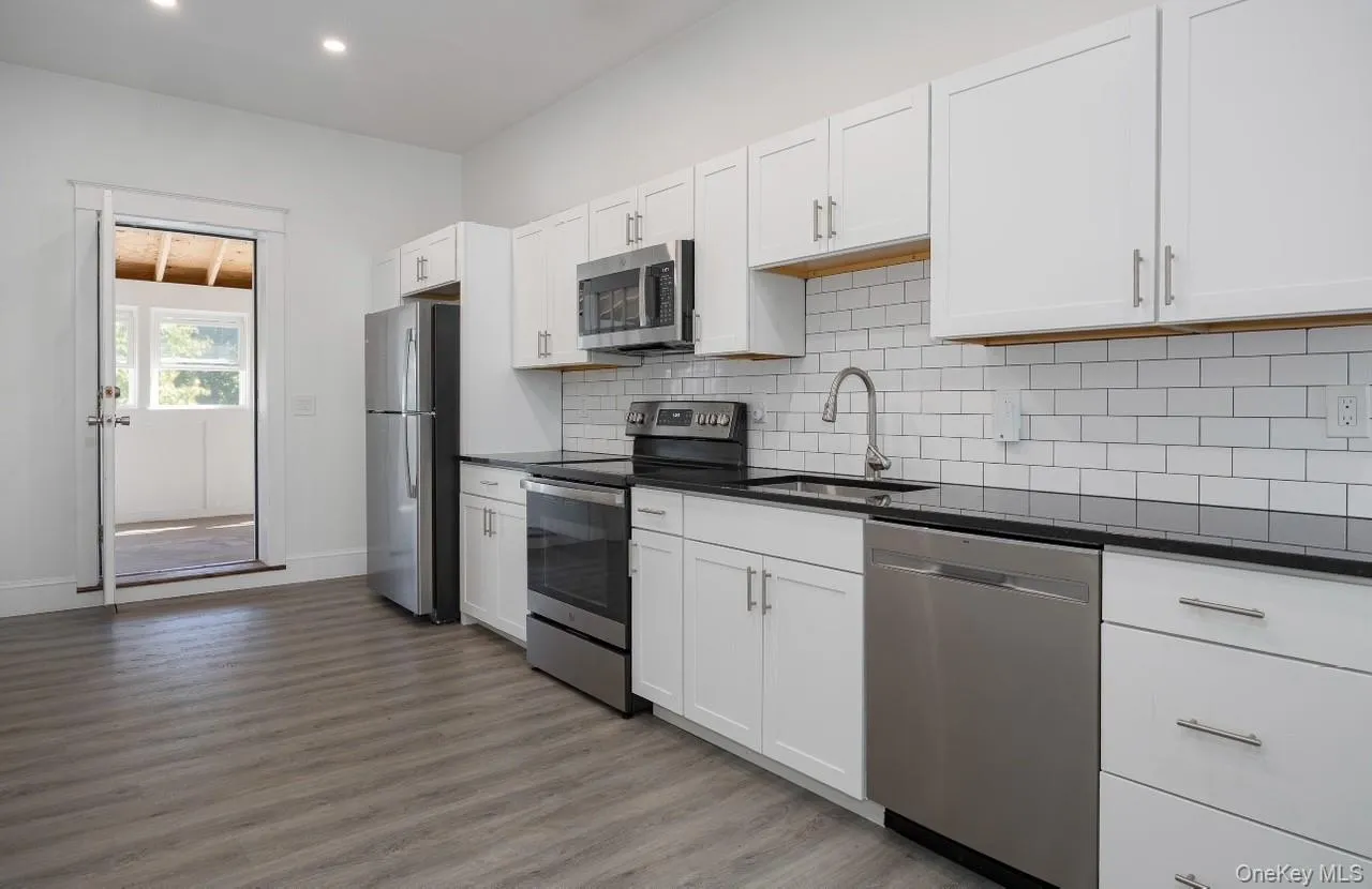 Kitchen with stainless steel appliances, white cabinetry, backsplash, light wood-style flooring, and dark stone counters Kitchen with stainless steel appliances, white cabinetry, backsplash, light wood-style flooring, and dark stone counters