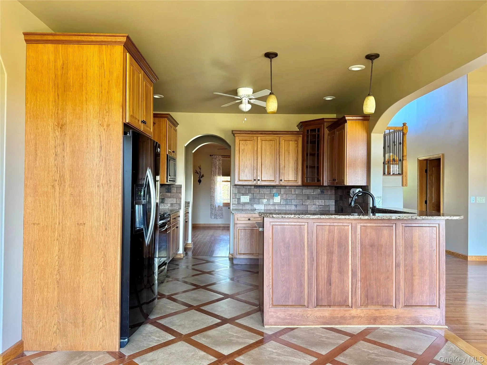 Kitchen featuring inlaid floor details, arched walkways, light stone counters, ceiling fan, and black appliances Kitchen featuring inlaid floor details, arched walkways, light stone counters, ceiling fan, and black appliances