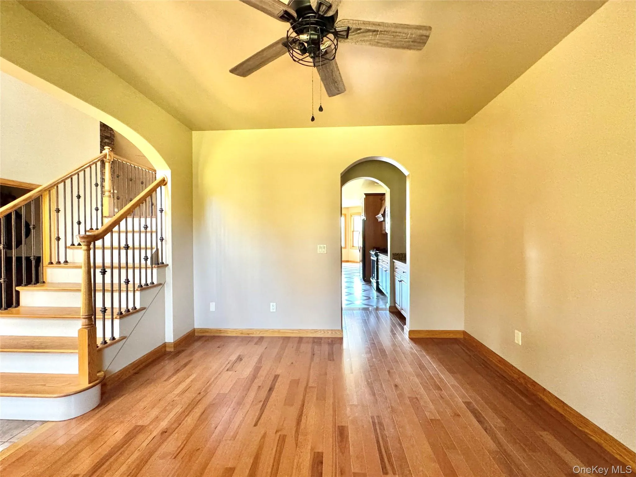 Unfurnished room with arched walkways, light wood finished floors, a ceiling fan, and stairs Unfurnished room with arched walkways, light wood finished floors, a ceiling fan, and stairs