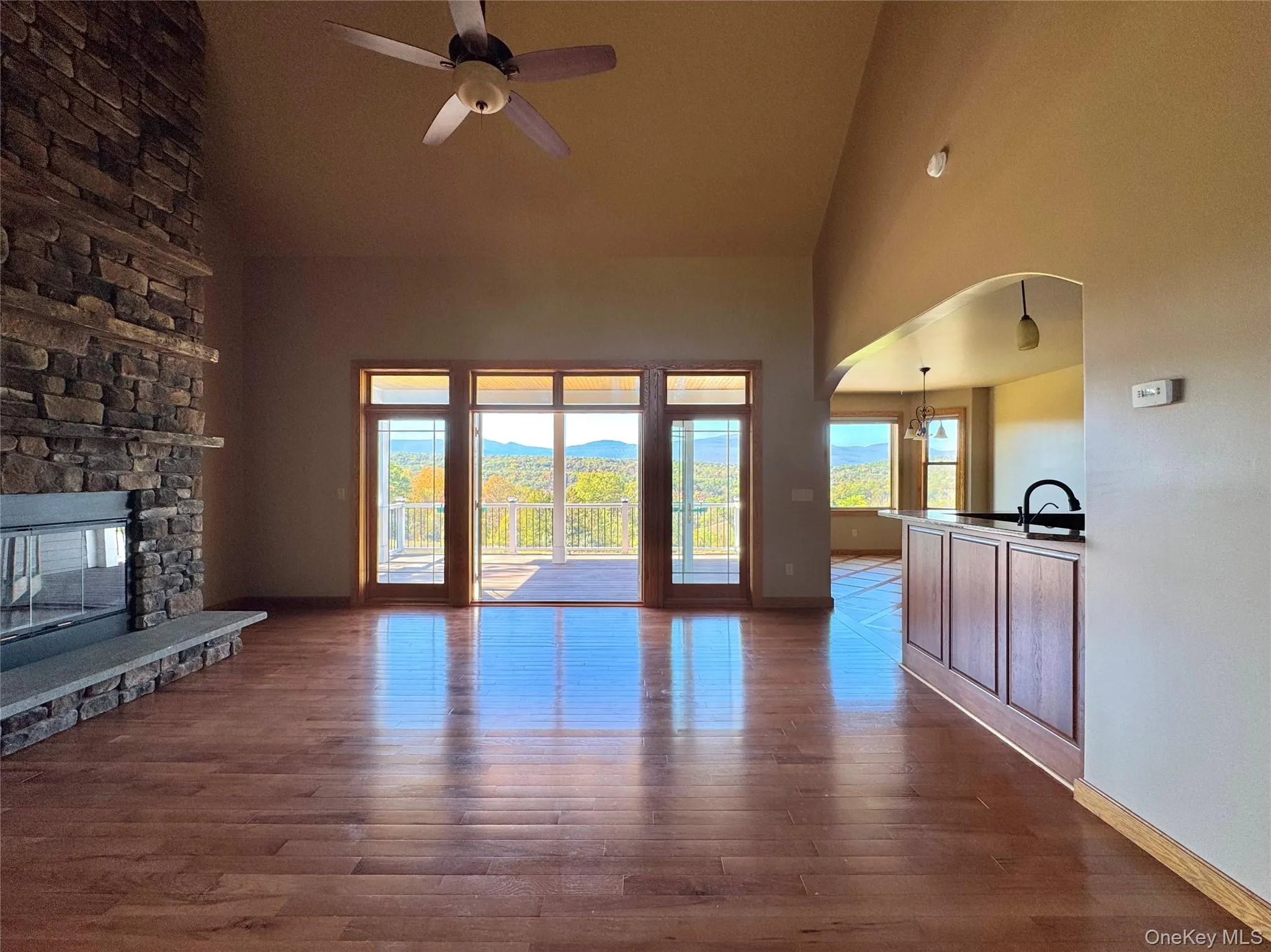 Unfurnished living room featuring high vaulted ceiling, dark wood-style floors, a stone fireplace, arched walkways, and a ceiling fan Unfurnished living room featuring high vaulted ceiling, dark wood-style floors, a stone fireplace, arched walkways, and a ceiling fan