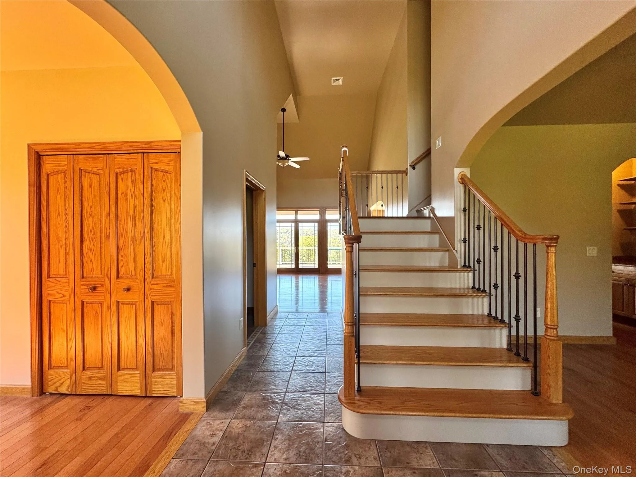 Stairway featuring arched walkways, wood finished floors, a high ceiling, and a ceiling fan Stairway featuring arched walkways, wood finished floors, a high ceiling, and a ceiling fan