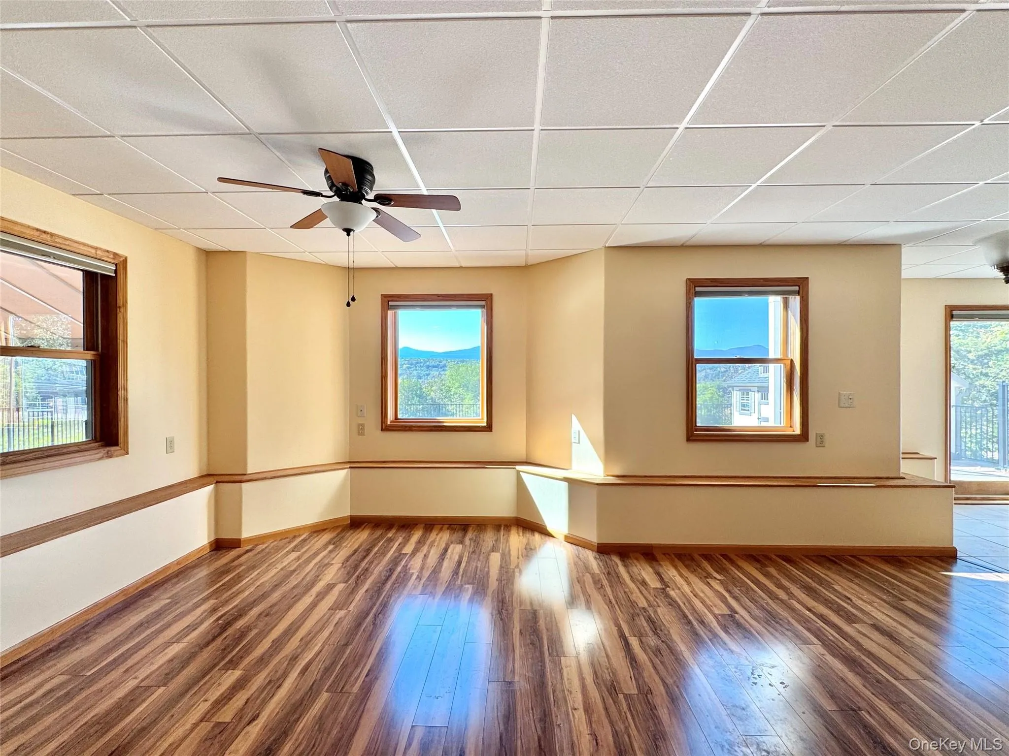 Unfurnished room with a ceiling fan, a paneled ceiling, and wood-type flooring Unfurnished room with a ceiling fan, a paneled ceiling, and wood-type flooring