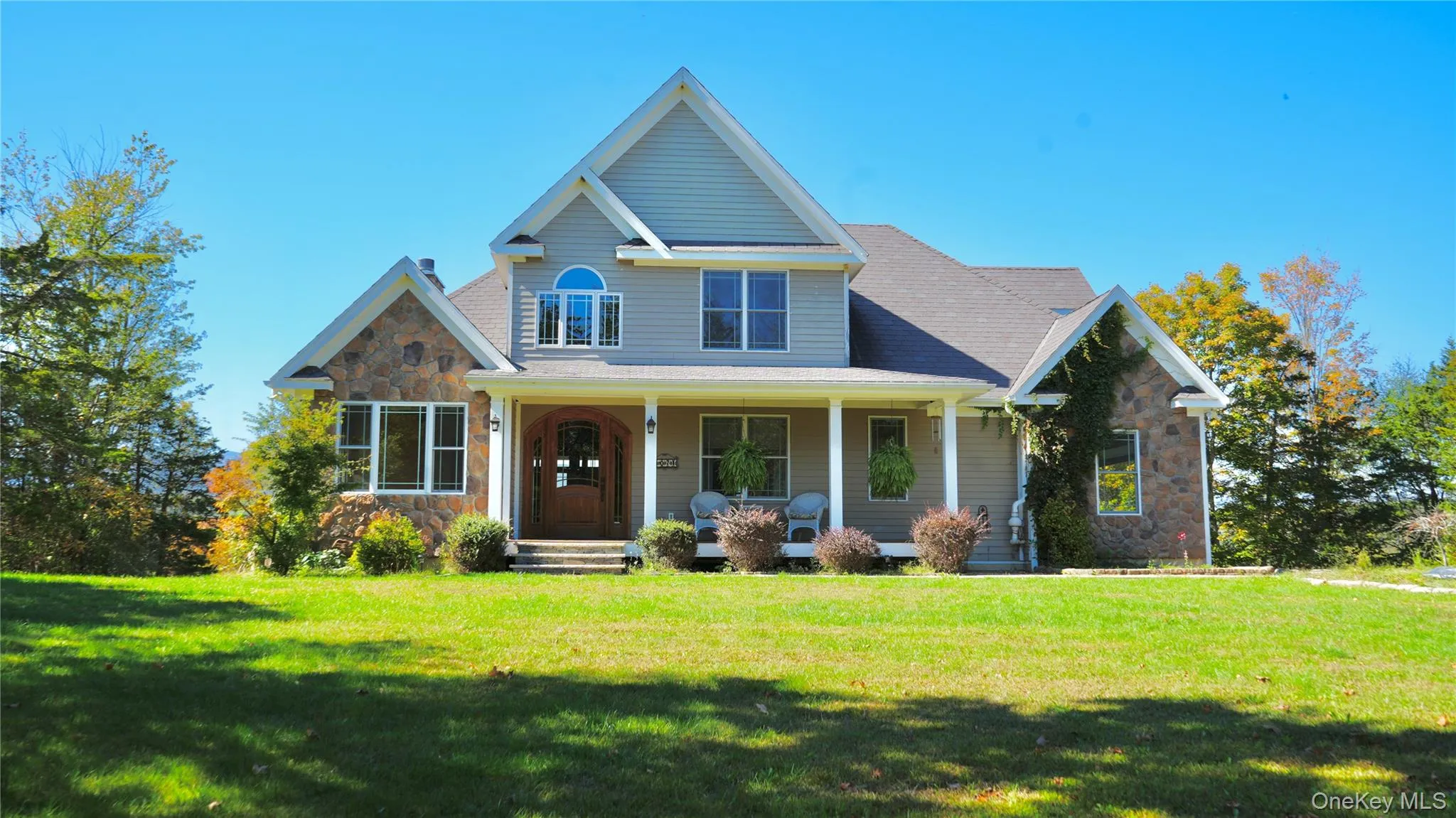 View of front of property featuring stone siding, covered porch, and a front lawn View of front of property featuring stone siding, covered porch, and a front lawn