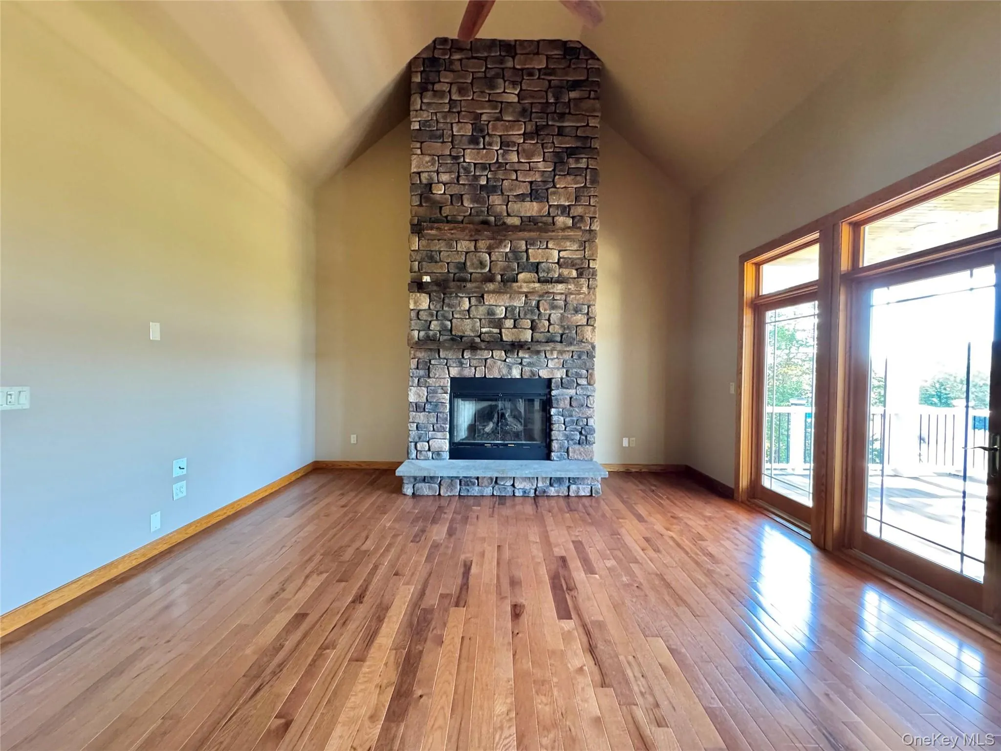 Unfurnished living room featuring hardwood / wood-style floors, a stone fireplace, and high vaulted ceiling Unfurnished living room featuring hardwood / wood-style floors, a stone fireplace, and high vaulted ceiling