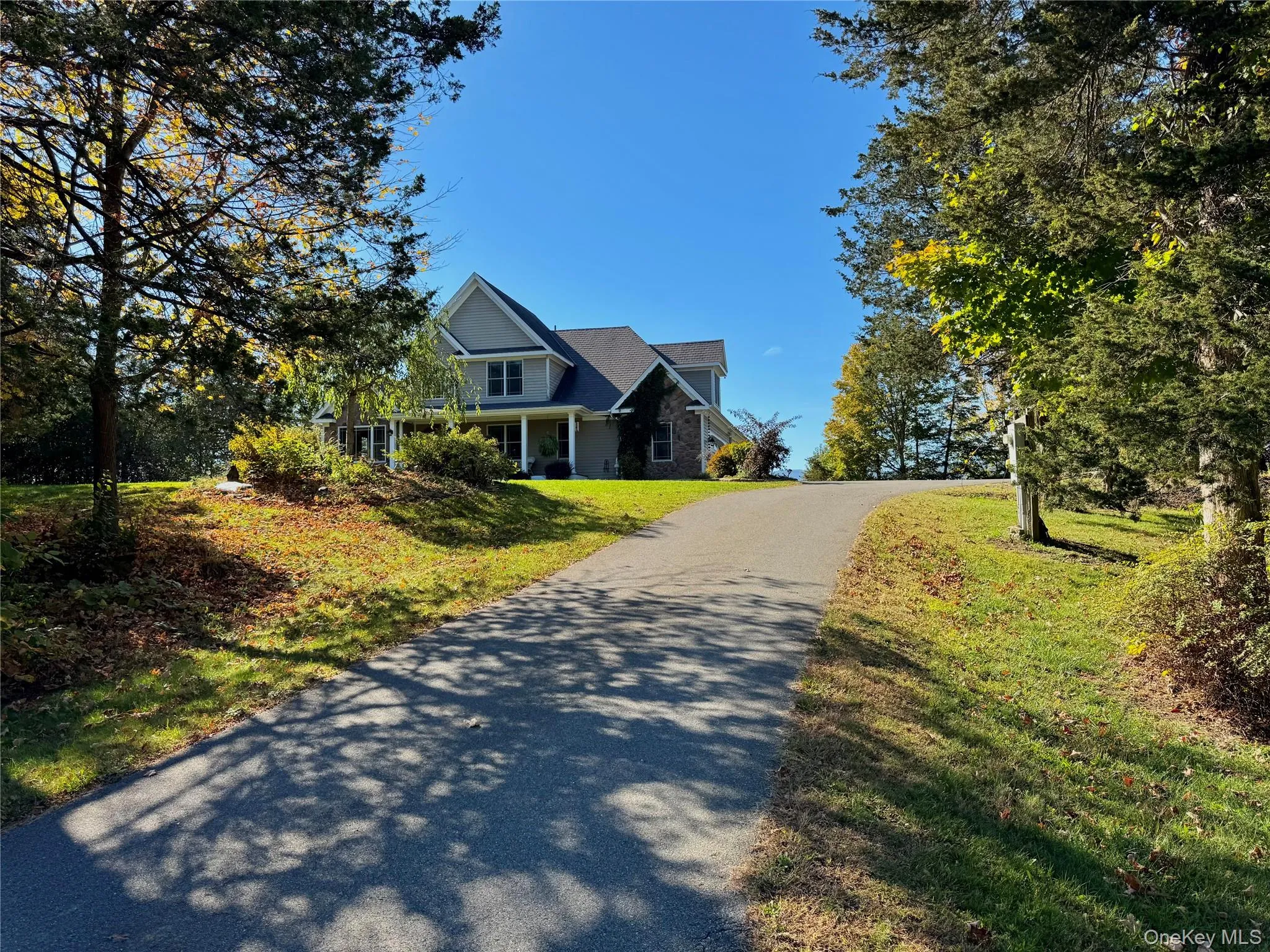 View of front facade featuring driveway, stone siding, a front yard, and covered porch View of front facade featuring driveway, stone siding, a front yard, and covered porch