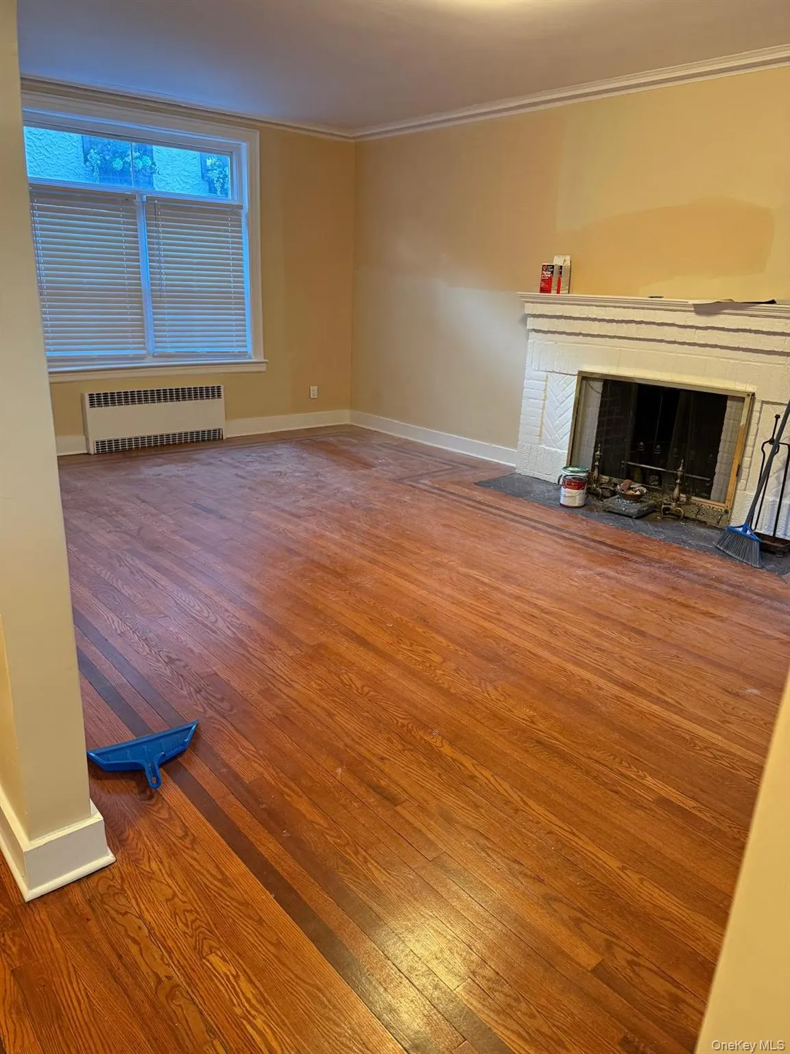 Unfurnished living room featuring wood-type flooring, radiator, a fireplace, and crown molding Unfurnished living room featuring wood-type flooring, radiator, a fireplace, and crown molding