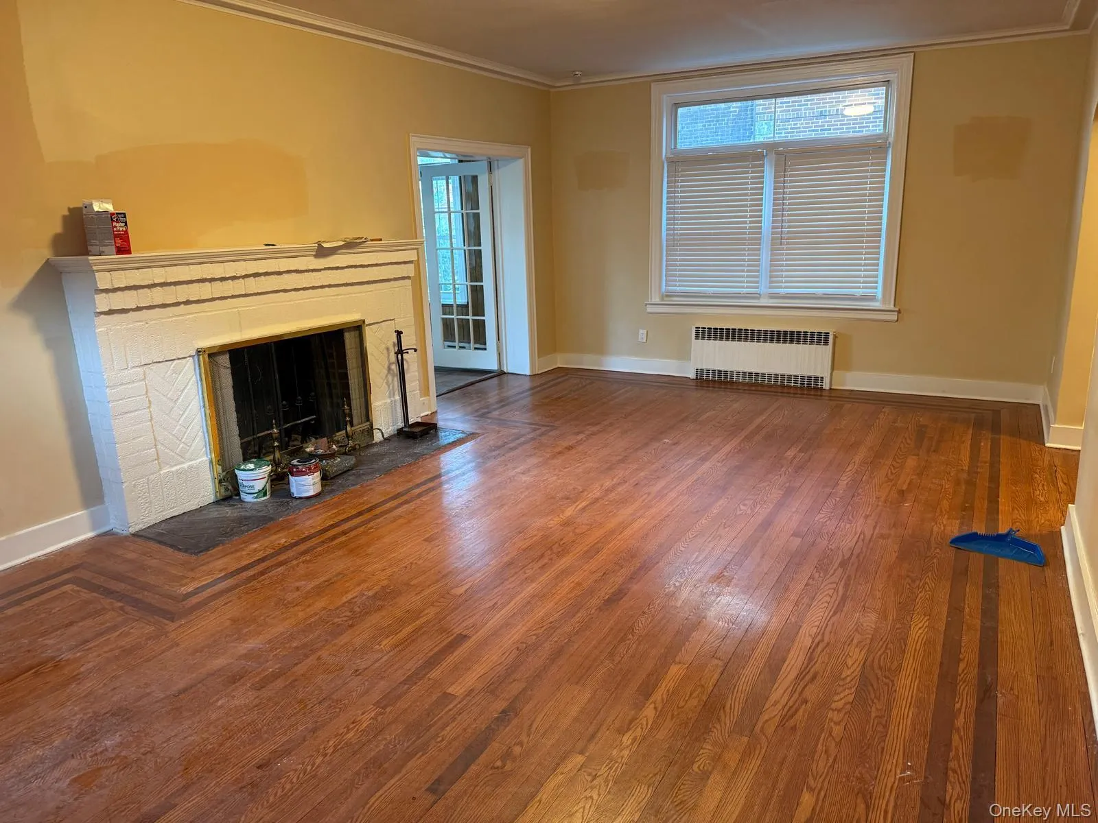 Unfurnished living room with a brick fireplace, radiator heating unit, wood-type flooring, healthy amount of natural light, and ornamental molding Unfurnished living room with a brick fireplace, radiator heating unit, wood-type flooring, healthy amount of natural light, and ornamental molding
