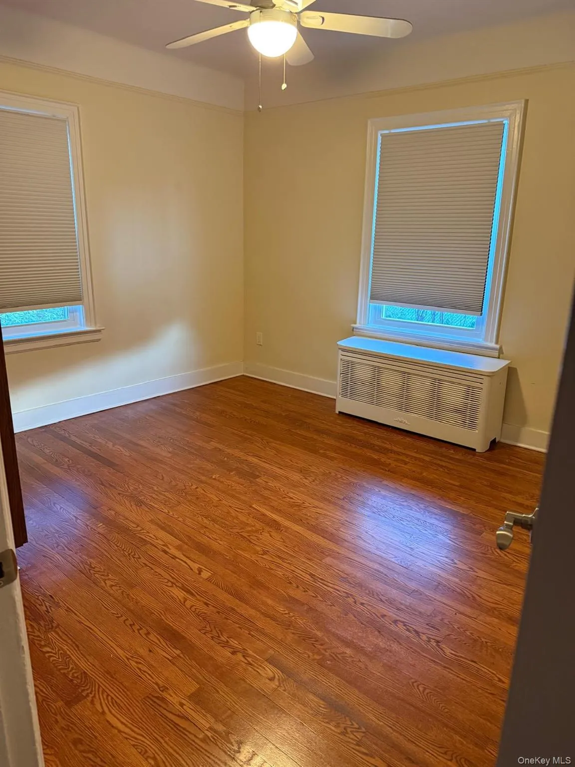 Empty room featuring dark wood-type flooring, radiator heating unit, and ceiling fan Empty room featuring dark wood-type flooring, radiator heating unit, and ceiling fan