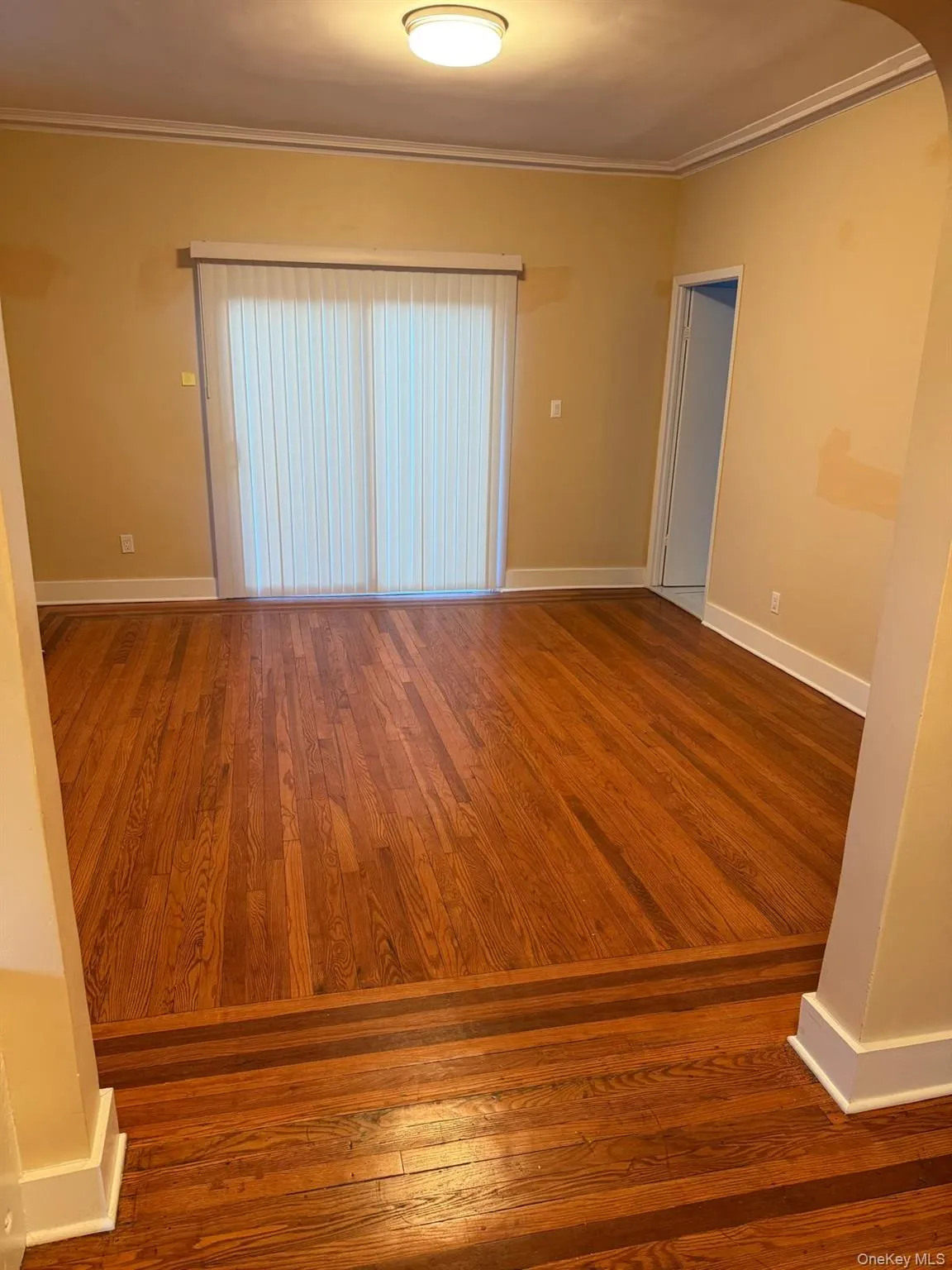 Empty room with dark wood-style floors, crown molding, and arched walkways Empty room with dark wood-style floors, crown molding, and arched walkways