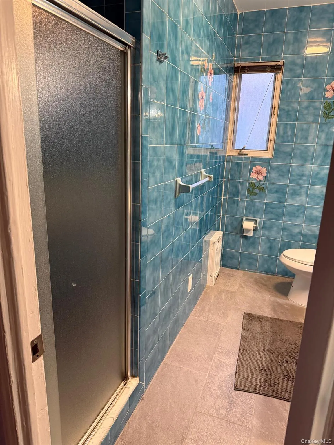 Bathroom featuring tile walls, tile patterned floors, a stall shower, and radiator heating unit Bathroom featuring tile walls, tile patterned floors, a stall shower, and radiator heating unit