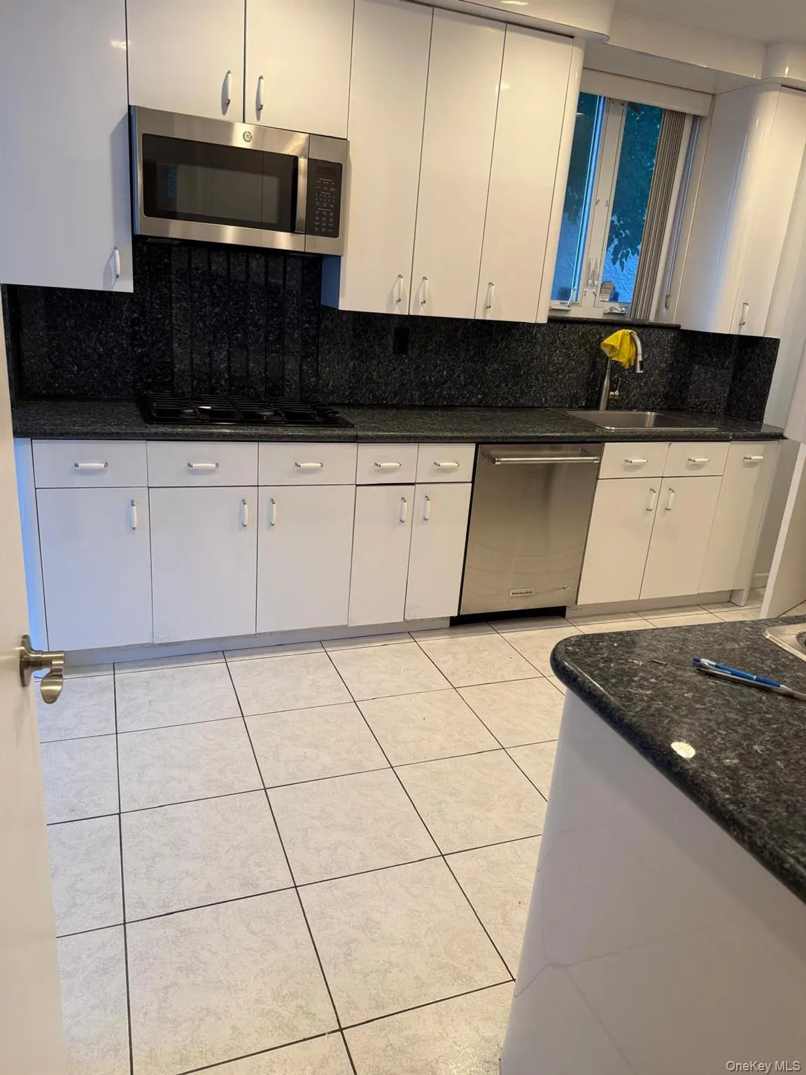 Kitchen featuring tasteful backsplash, dark stone countertops, stainless steel appliances, light tile patterned floors, and white cabinetry Kitchen featuring tasteful backsplash, dark stone countertops, stainless steel appliances, light tile patterned floors, and white cabinetry