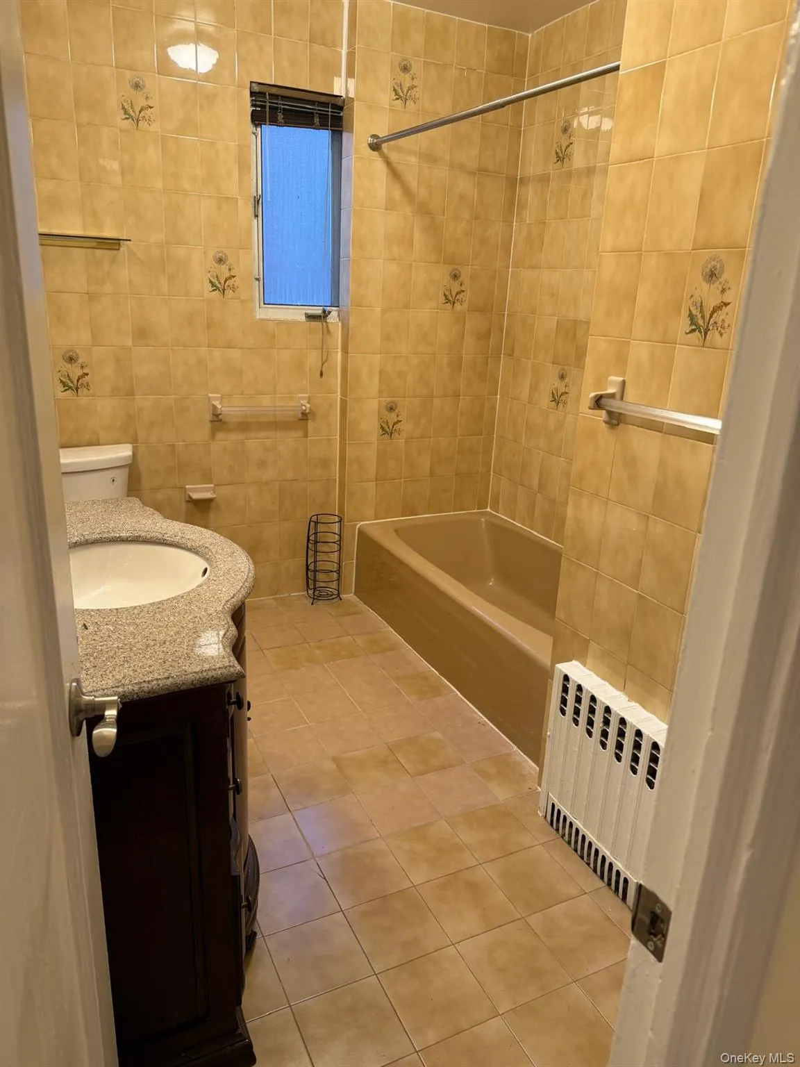 Full bath with vanity, light tile patterned floors, radiator, tile walls, and tub / shower combination Full bath with vanity, light tile patterned floors, radiator, tile walls, and tub / shower combination