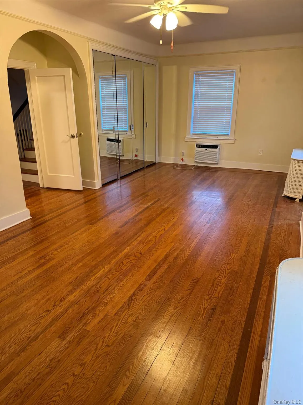 Unfurnished living room featuring dark wood-style flooring, a ceiling fan, and arched walkways Unfurnished living room featuring dark wood-style flooring, a ceiling fan, and arched walkways