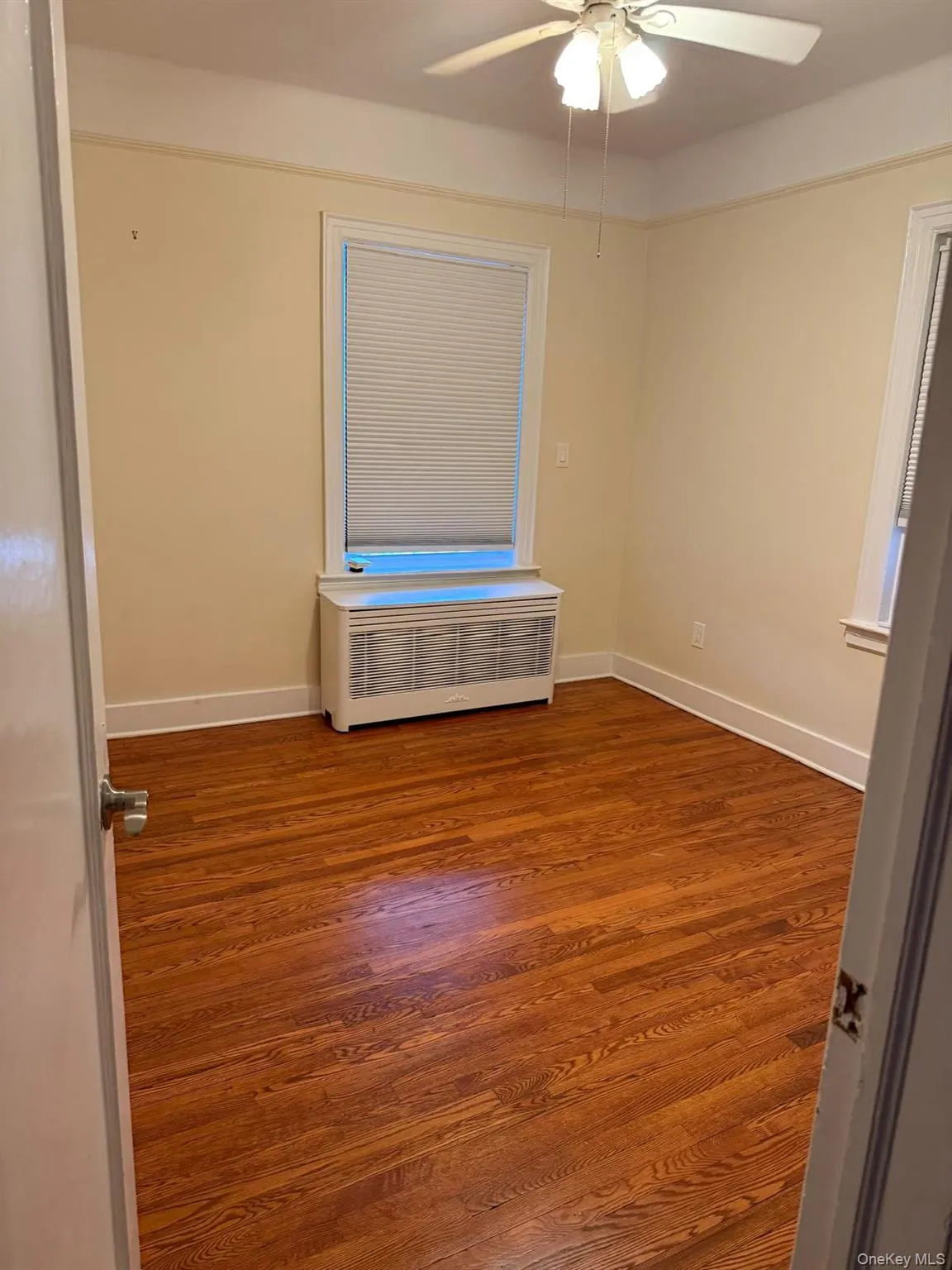 Empty room with dark wood finished floors, a ceiling fan, and radiator Empty room with dark wood finished floors, a ceiling fan, and radiator