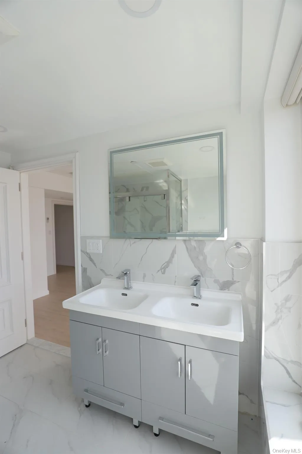 Full bathroom featuring light marble finish floors, double vanity, and tile walls Full bathroom featuring light marble finish floors, double vanity, and tile walls