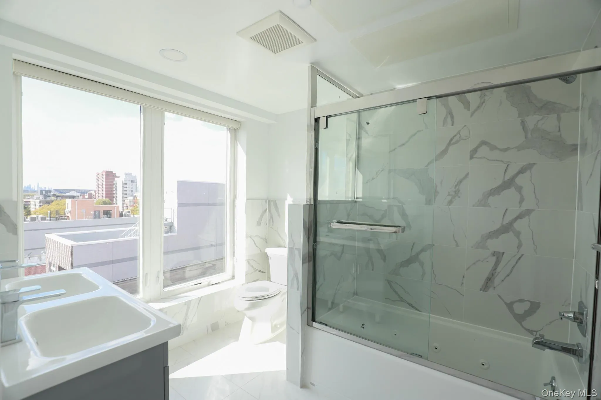 Bathroom with shower / bath combination with glass door, double vanity, a city view, light marble finish floors, and tile walls Bathroom with shower / bath combination with glass door, double vanity, a city view, light marble finish floors, and tile walls
