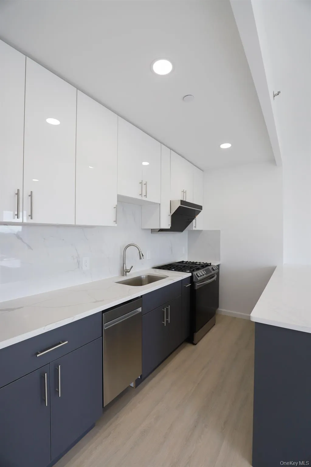 Kitchen with white cabinetry, modern cabinets, light wood-style floors, appliances with stainless steel finishes, and light stone counters Kitchen with white cabinetry, modern cabinets, light wood-style floors, appliances with stainless steel finishes, and light stone counters