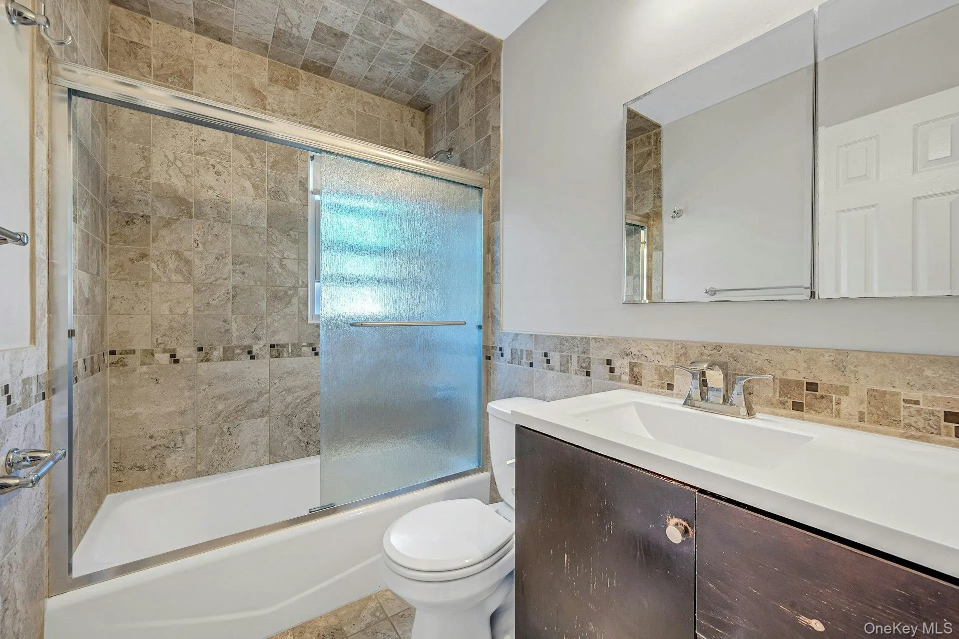 Full bath featuring combined bath / shower with glass door, vanity, tile walls, and light tile patterned floors Full bath featuring combined bath / shower with glass door, vanity, tile walls, and light tile patterned floors