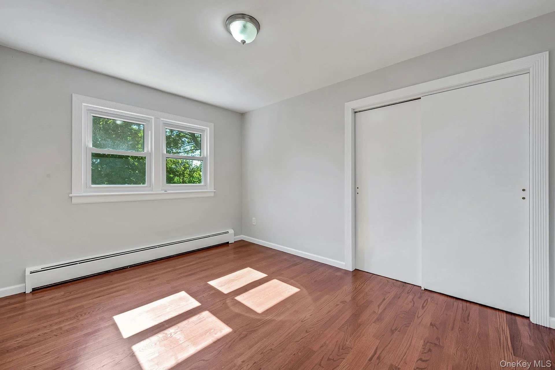 Unfurnished bedroom featuring baseboard heating, wood finished floors, and a closet Unfurnished bedroom featuring baseboard heating, wood finished floors, and a closet