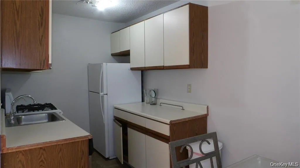 Kitchen with light countertops, white cabinets, freestanding refrigerator, brown cabinetry, and a textured ceiling Kitchen with light countertops, white cabinets, freestanding refrigerator, brown cabinetry, and a textured ceiling