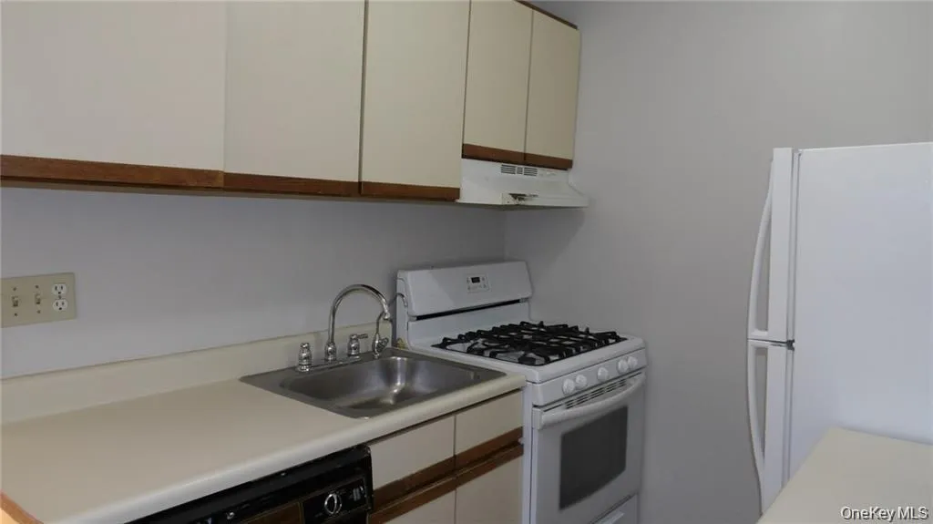 Kitchen with white appliances, light countertops, under cabinet range hood, white cabinetry, and brown cabinetry Kitchen with white appliances, light countertops, under cabinet range hood, white cabinetry, and brown cabinetry