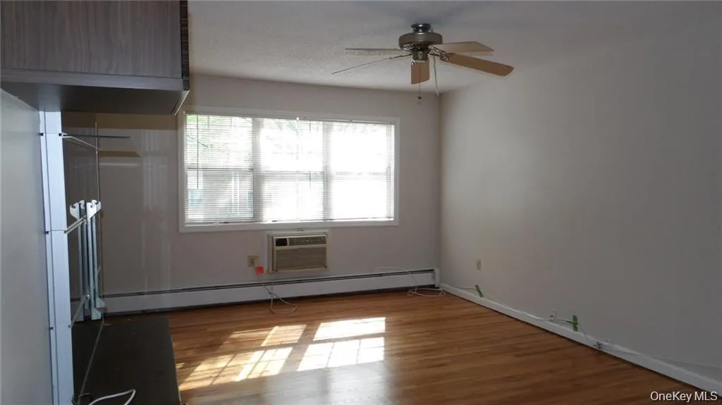 Unfurnished bedroom featuring a baseboard heating unit, light wood-style floors, a ceiling fan, and a wall unit AC Unfurnished bedroom featuring a baseboard heating unit, light wood-style floors, a ceiling fan, and a wall unit AC