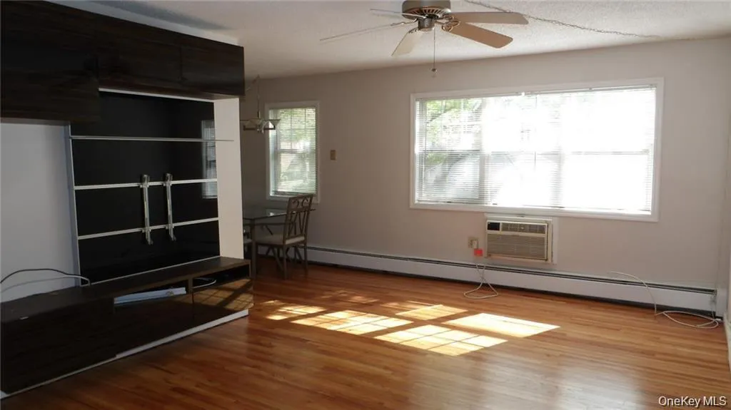 Unfurnished living room with light wood finished floors, baseboard heating, a ceiling fan, and a wall mounted AC Unfurnished living room with light wood finished floors, baseboard heating, a ceiling fan, and a wall mounted AC