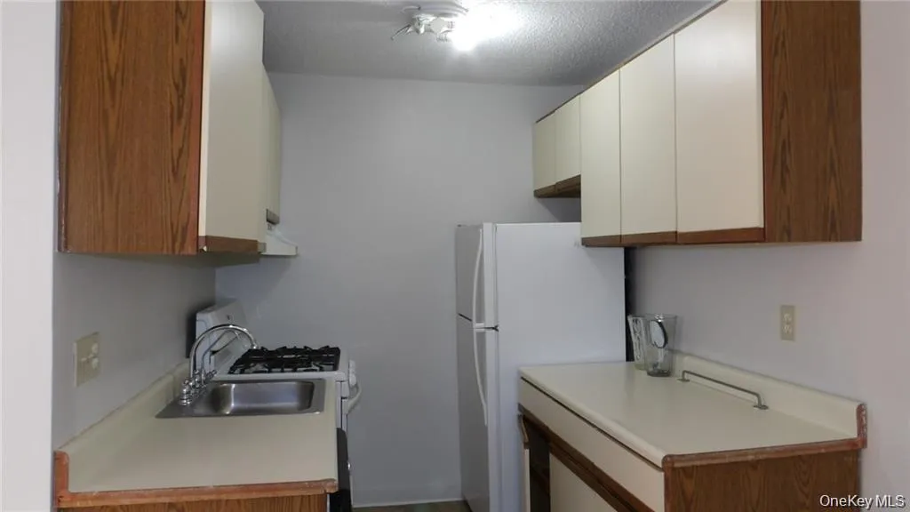 Kitchen featuring light countertops, white appliances, brown cabinets, and a textured ceiling Kitchen featuring light countertops, white appliances, brown cabinets, and a textured ceiling