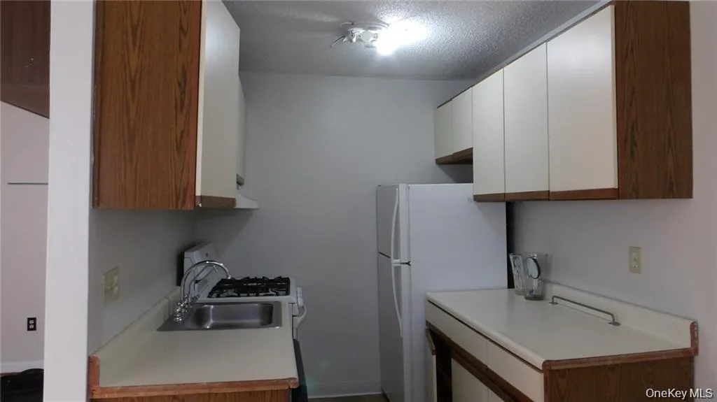 Kitchen with light countertops, white cabinets, white appliances, a textured ceiling, and brown cabinets Kitchen with light countertops, white cabinets, white appliances, a textured ceiling, and brown cabinets
