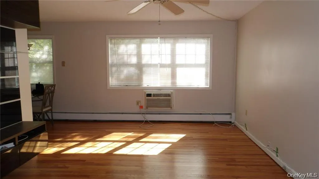 Unfurnished living room with wood finished floors, ceiling fan, and an AC wall unit Unfurnished living room with wood finished floors, ceiling fan, and an AC wall unit