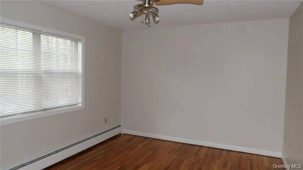 Empty room featuring baseboard heating, dark wood-type flooring, and ceiling fan Empty room featuring baseboard heating, dark wood-type flooring, and ceiling fan