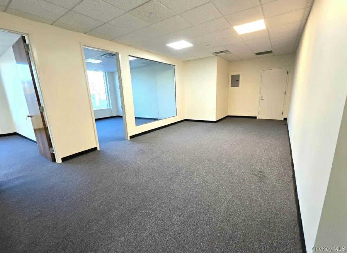 Unfurnished room with a paneled ceiling, dark carpet, and electric panel Unfurnished room with a paneled ceiling, dark carpet, and electric panel
