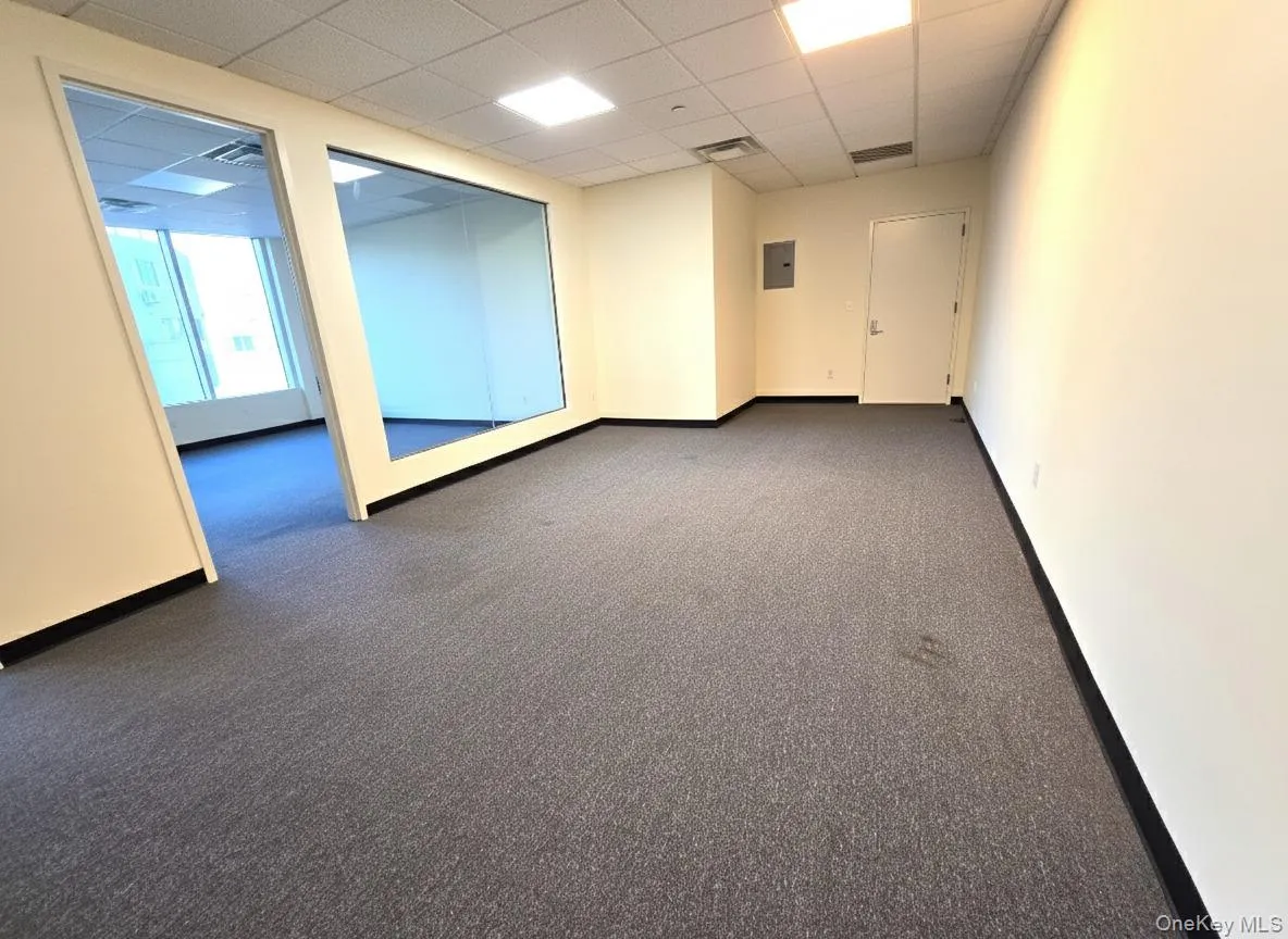Empty room with a paneled ceiling, dark colored carpet, and electric panel Empty room with a paneled ceiling, dark colored carpet, and electric panel