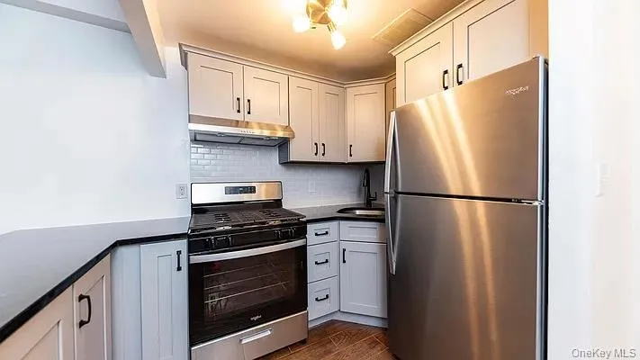Kitchen featuring stainless steel appliances, tasteful backsplash, dark wood-type flooring, under cabinet range hood, and dark stone counters Kitchen featuring stainless steel appliances, tasteful backsplash, dark wood-type flooring, under cabinet range hood, and dark stone counters