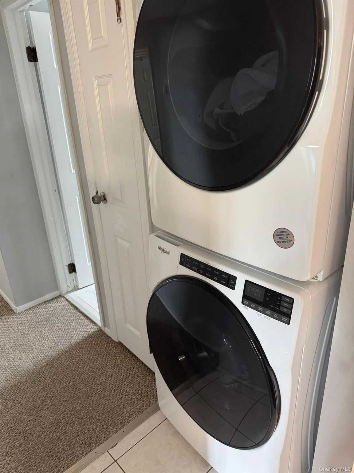 Washroom featuring light colored carpet, stacked washer / dryer, and light tile patterned floors Washroom featuring light colored carpet, stacked washer / dryer, and light tile patterned floors