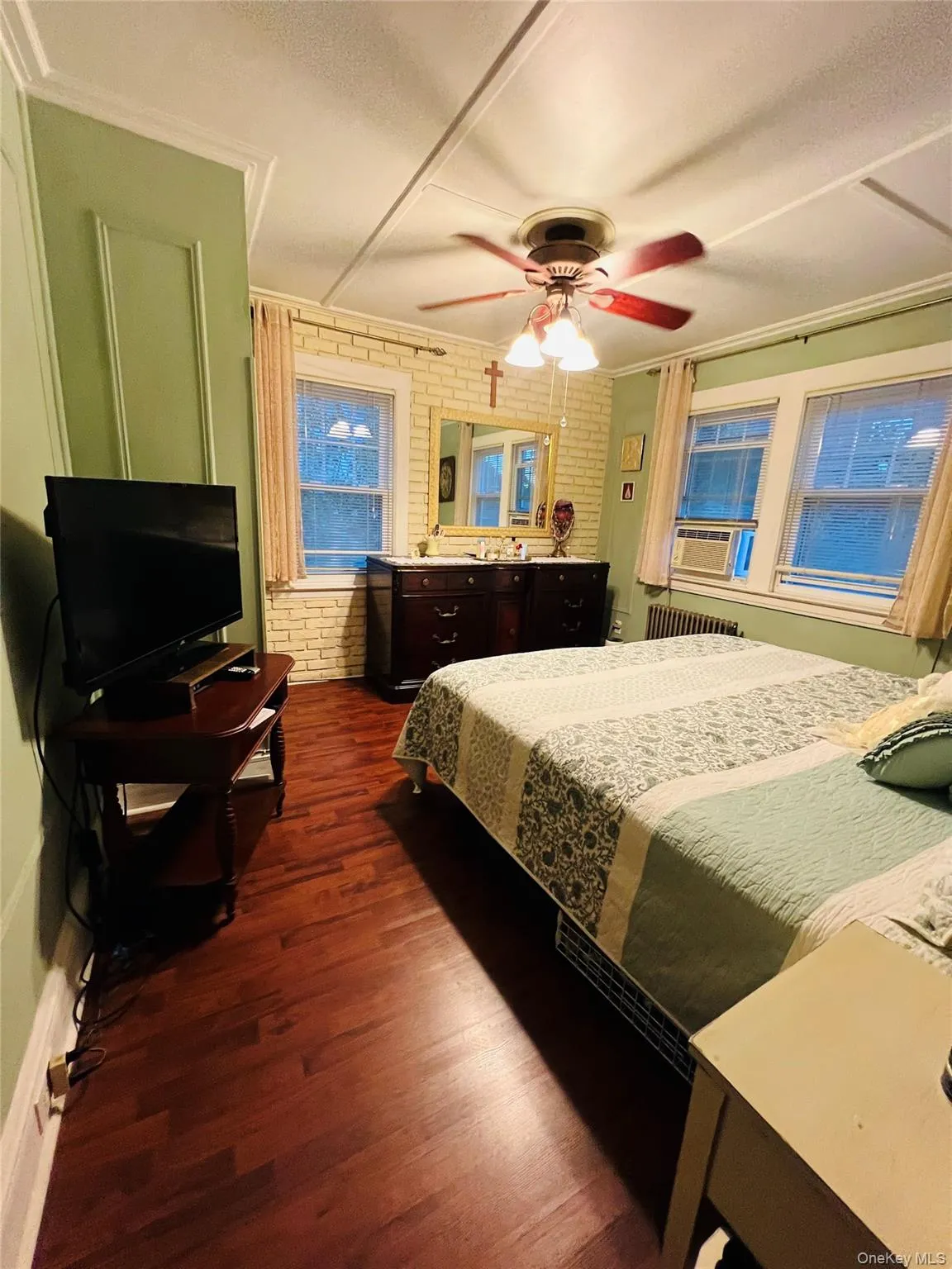 Bedroom with brick wall, dark wood-style floors, ceiling fan, ornamental molding, and cooling unit Bedroom with brick wall, dark wood-style floors, ceiling fan, ornamental molding, and cooling unit