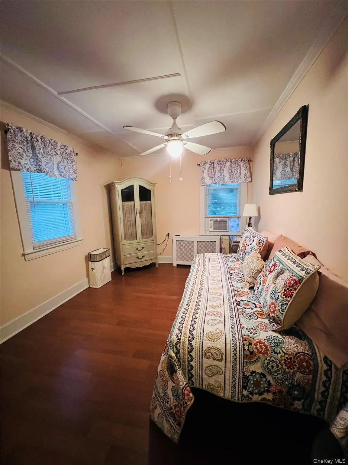 Bedroom with dark wood-style flooring, ceiling fan, radiator heating unit, and ornamental molding Bedroom with dark wood-style flooring, ceiling fan, radiator heating unit, and ornamental molding