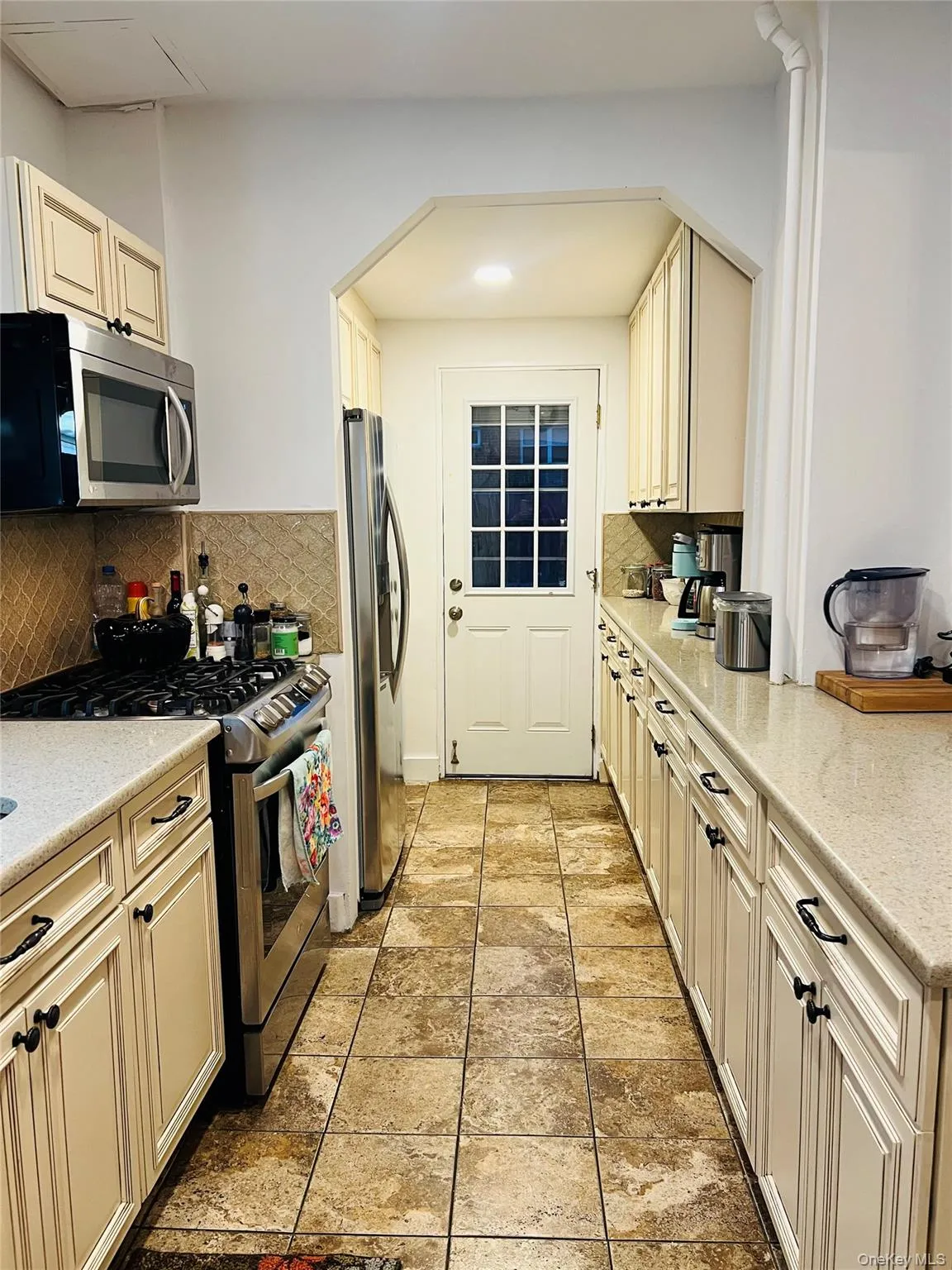 Kitchen with cream cabinets, appliances with stainless steel finishes, decorative backsplash, and light stone counters Kitchen with cream cabinets, appliances with stainless steel finishes, decorative backsplash, and light stone counters