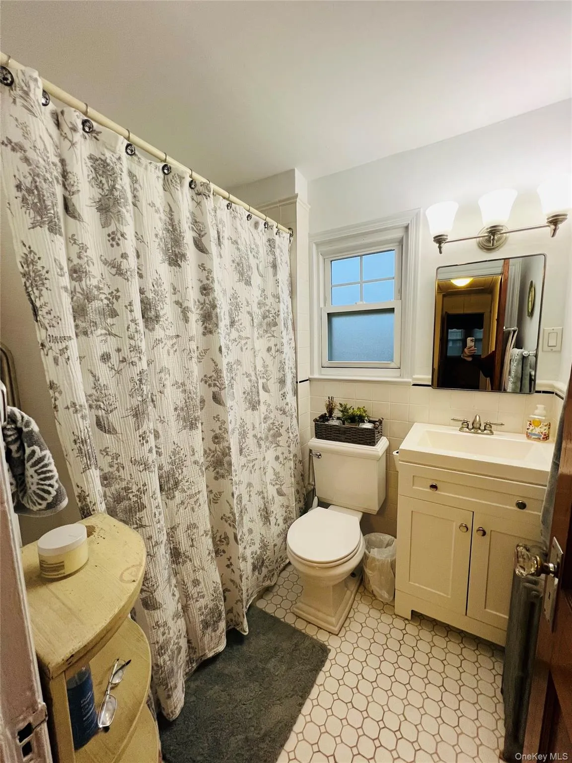 Full bath with vanity, tile walls, light tile patterned floors, a shower with shower curtain, and wainscoting Full bath with vanity, tile walls, light tile patterned floors, a shower with shower curtain, and wainscoting