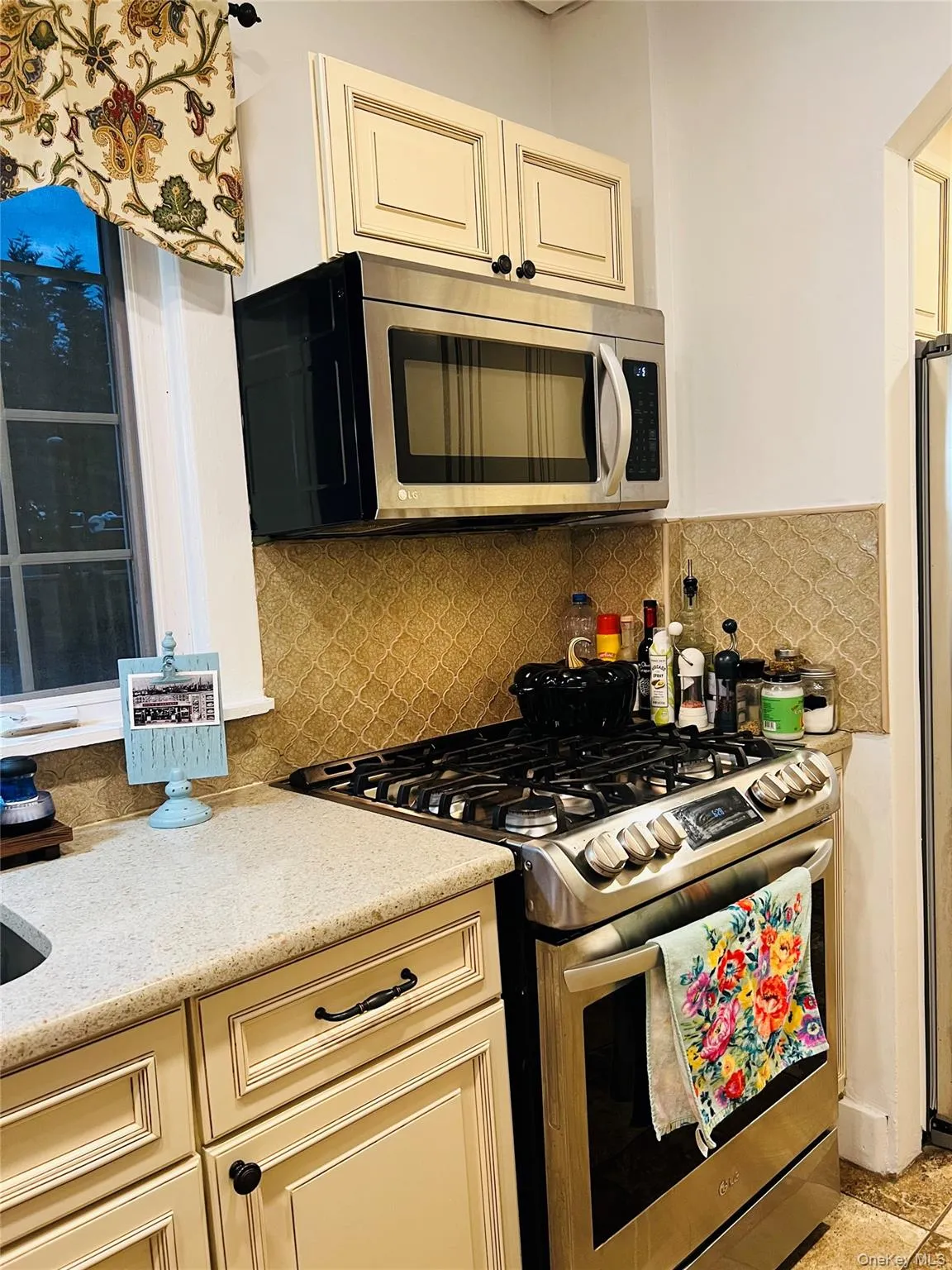 Kitchen featuring appliances with stainless steel finishes, cream cabinets, backsplash, and light stone counters Kitchen featuring appliances with stainless steel finishes, cream cabinets, backsplash, and light stone counters