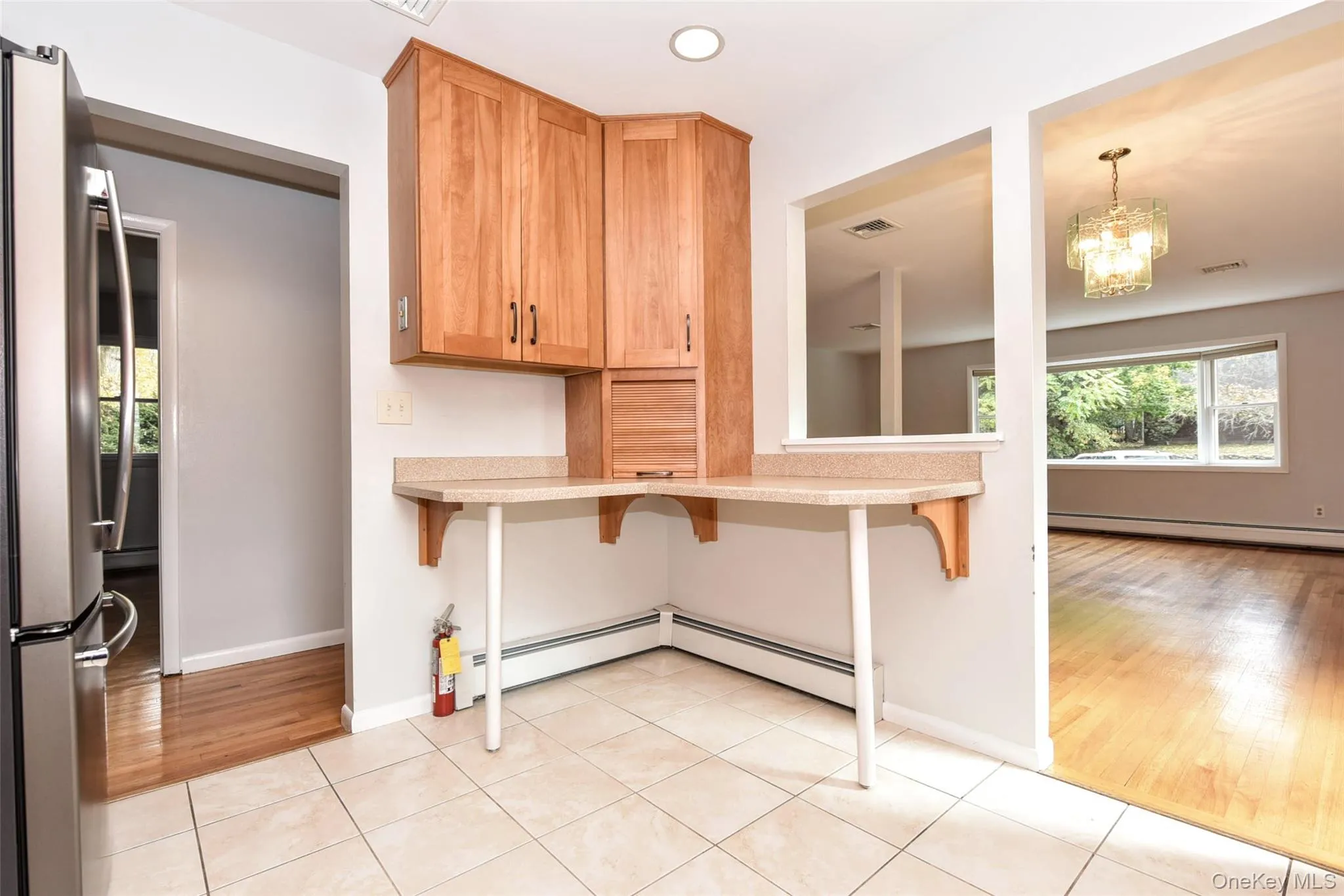 Kitchen with light tile patterned floors, freestanding refrigerator, a breakfast bar area, a baseboard radiator, and a chandelier Kitchen with light tile patterned floors, freestanding refrigerator, a breakfast bar area, a baseboard radiator, and a chandelier