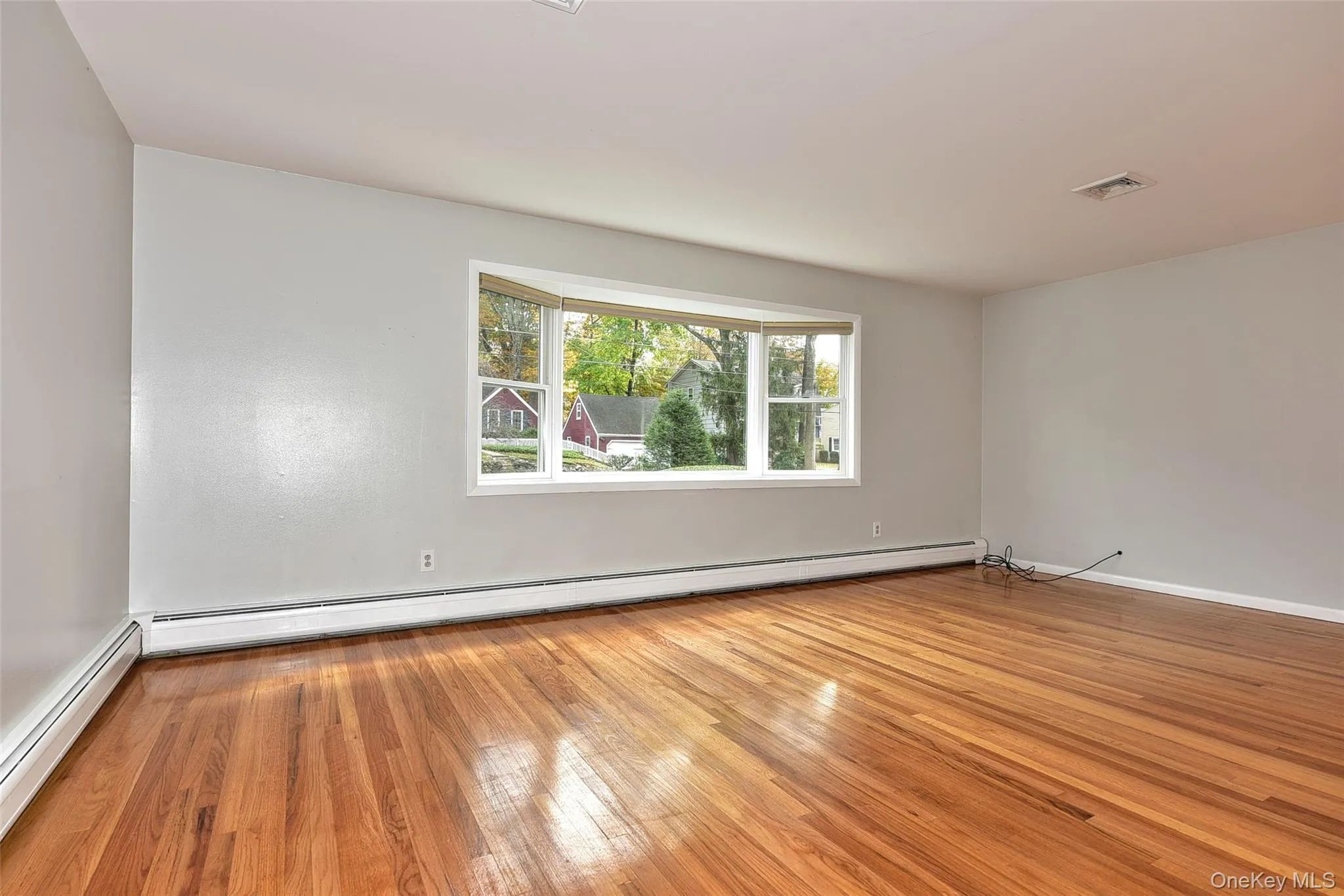 Empty room with light wood-type flooring, a baseboard radiator, and a baseboard heating unit Empty room with light wood-type flooring, a baseboard radiator, and a baseboard heating unit