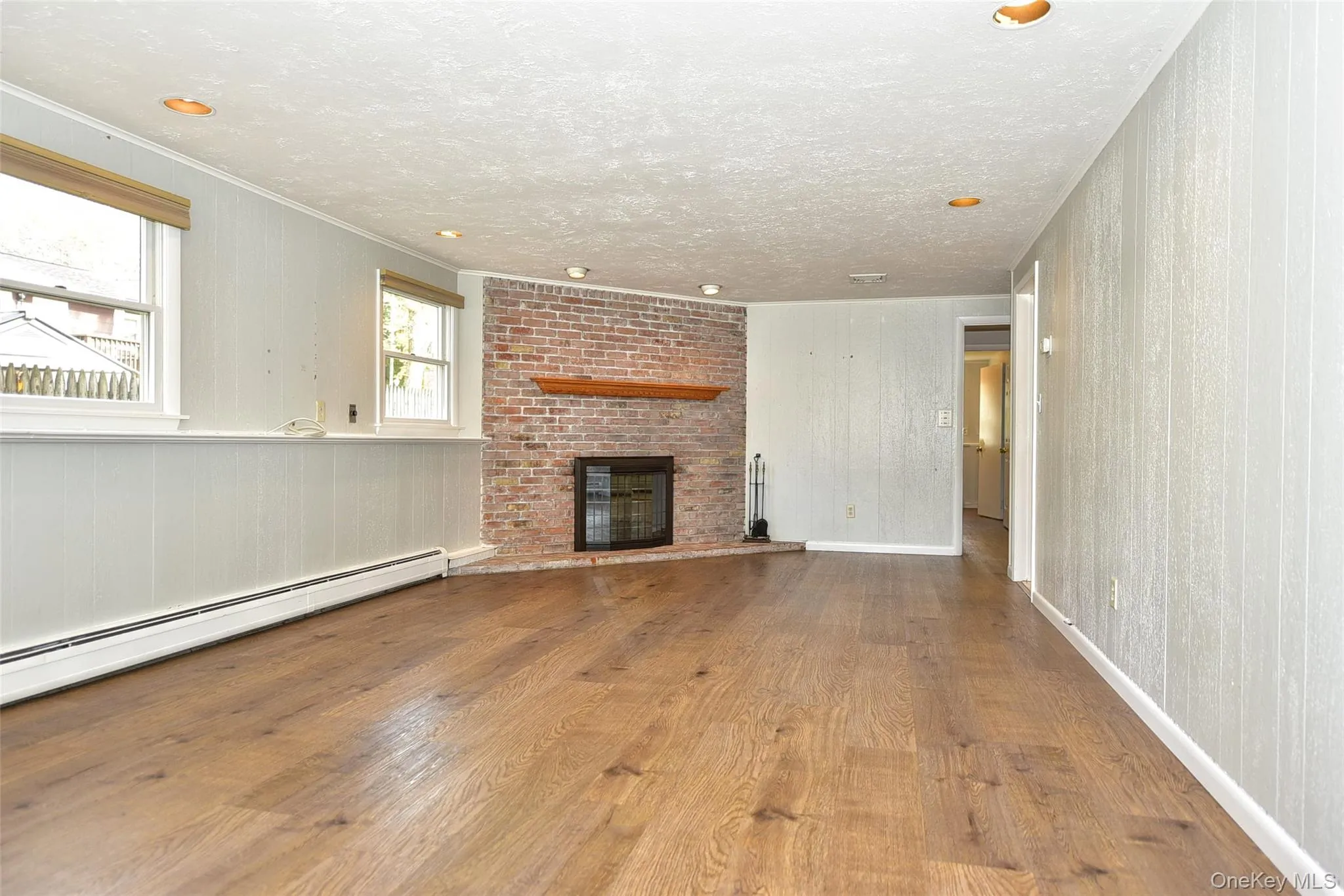 Unfurnished living room featuring wood finished floors, a fireplace, baseboard heating, crown molding, and a textured ceiling Unfurnished living room featuring wood finished floors, a fireplace, baseboard heating, crown molding, and a textured ceiling