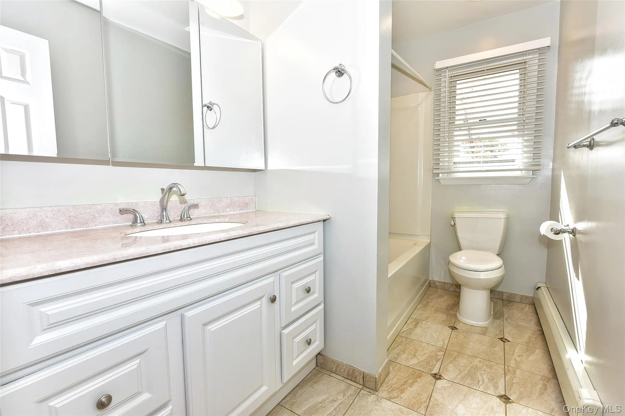 Full bathroom with a baseboard heating unit, vanity, bathing tub / shower combination, and light tile patterned flooring Full bathroom with a baseboard heating unit, vanity, bathing tub / shower combination, and light tile patterned flooring