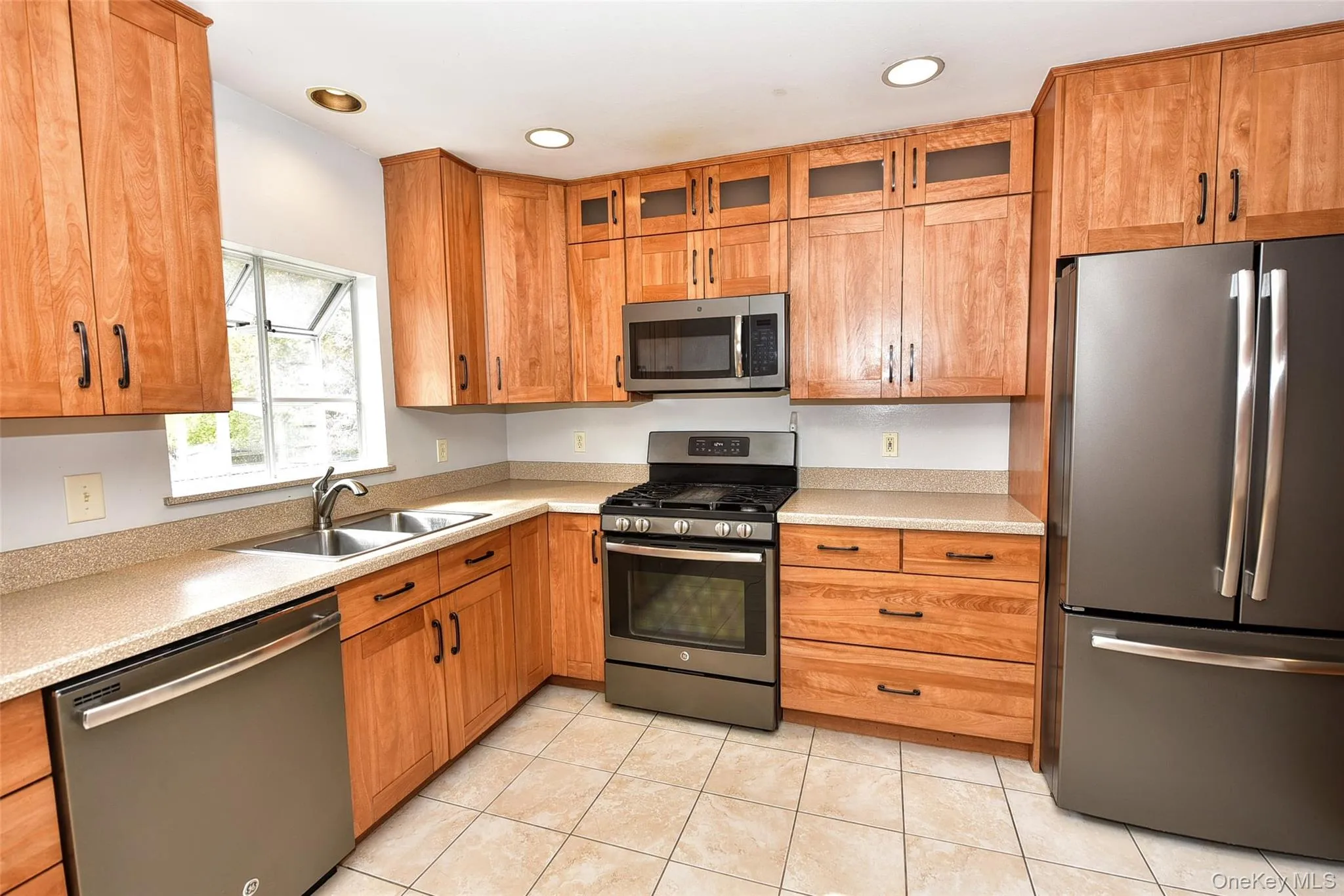 Kitchen with stainless steel appliances, glass insert cabinets, light countertops, light tile patterned floors, and recessed lighting Kitchen with stainless steel appliances, glass insert cabinets, light countertops, light tile patterned floors, and recessed lighting