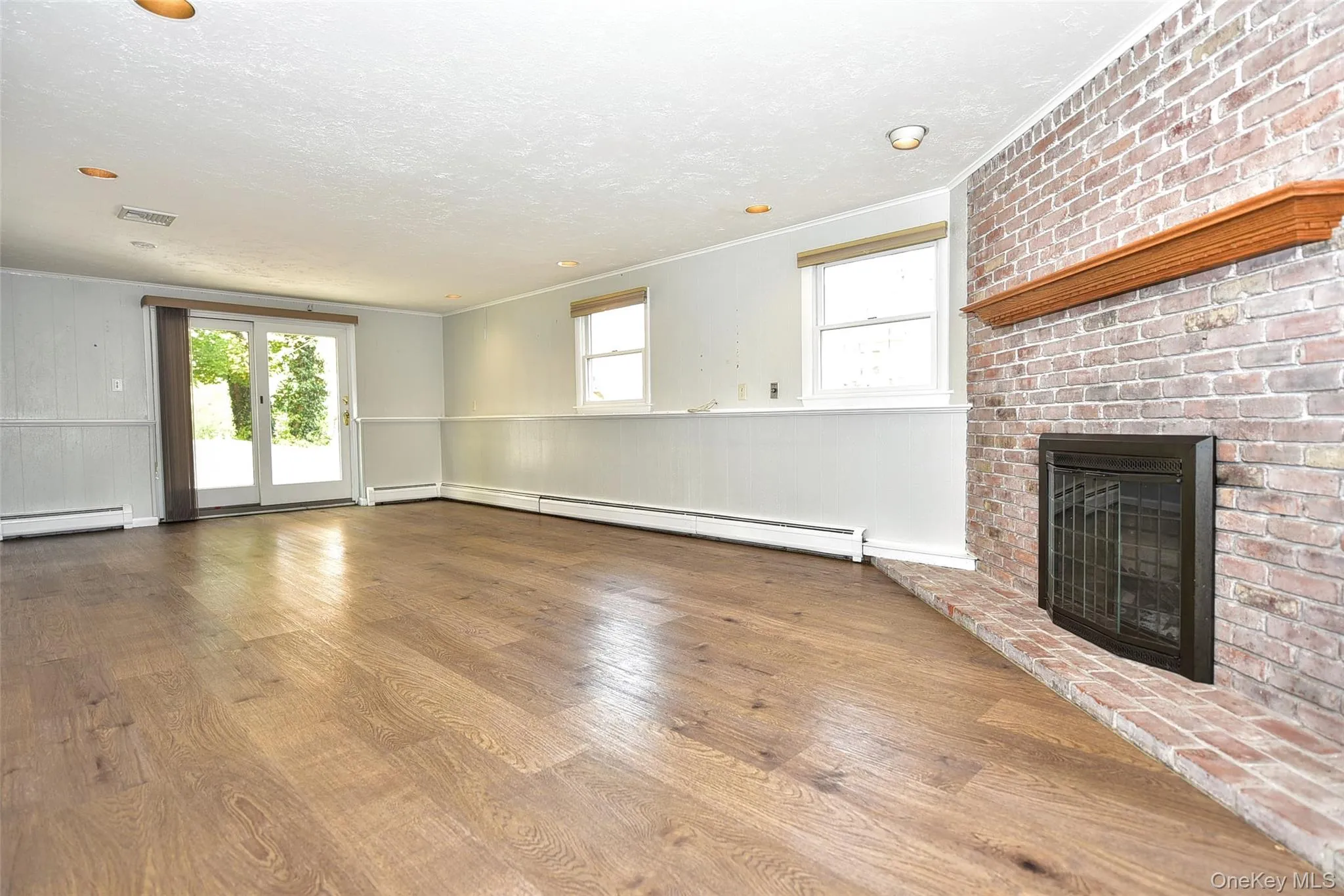 Unfurnished living room with crown molding, wood finished floors, a fireplace, plenty of natural light, and a baseboard radiator Unfurnished living room with crown molding, wood finished floors, a fireplace, plenty of natural light, and a baseboard radiator