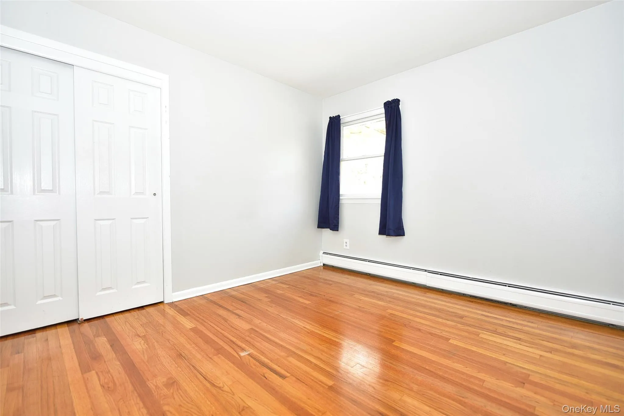Unfurnished bedroom featuring a baseboard heating unit, light wood-type flooring, and a closet Unfurnished bedroom featuring a baseboard heating unit, light wood-type flooring, and a closet