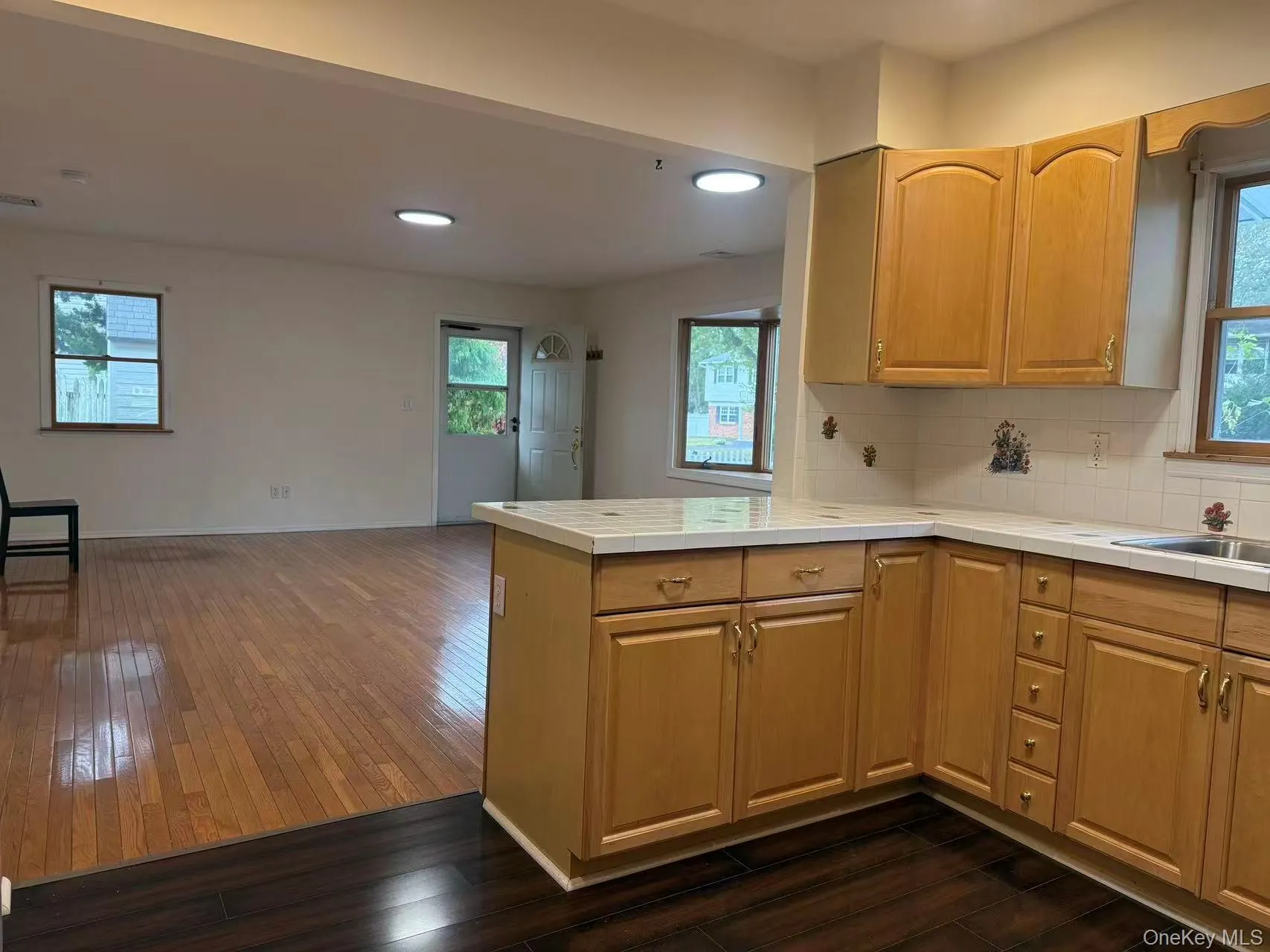 Kitchen with tile counters, decorative backsplash, dark wood finished floors, open floor plan, and a peninsula Kitchen with tile counters, decorative backsplash, dark wood finished floors, open floor plan, and a peninsula