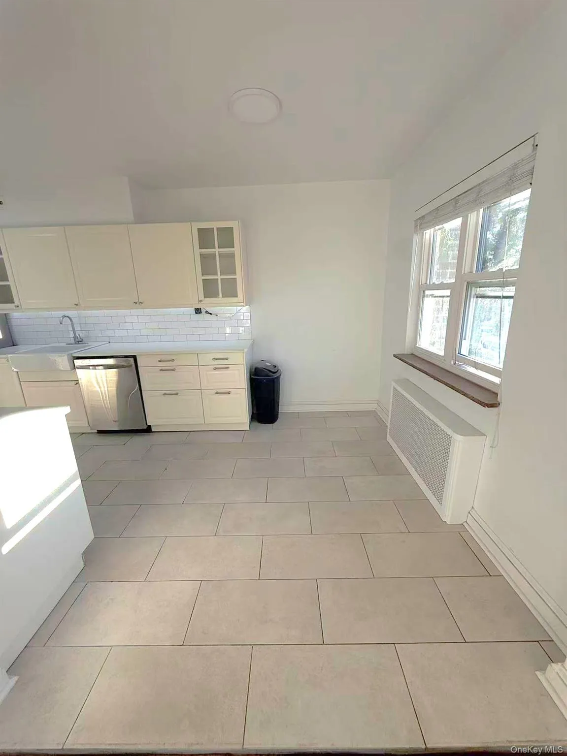 Kitchen featuring tasteful backsplash, radiator, dishwasher, light tile patterned flooring, and glass insert cabinets Kitchen featuring tasteful backsplash, radiator, dishwasher, light tile patterned flooring, and glass insert cabinets
